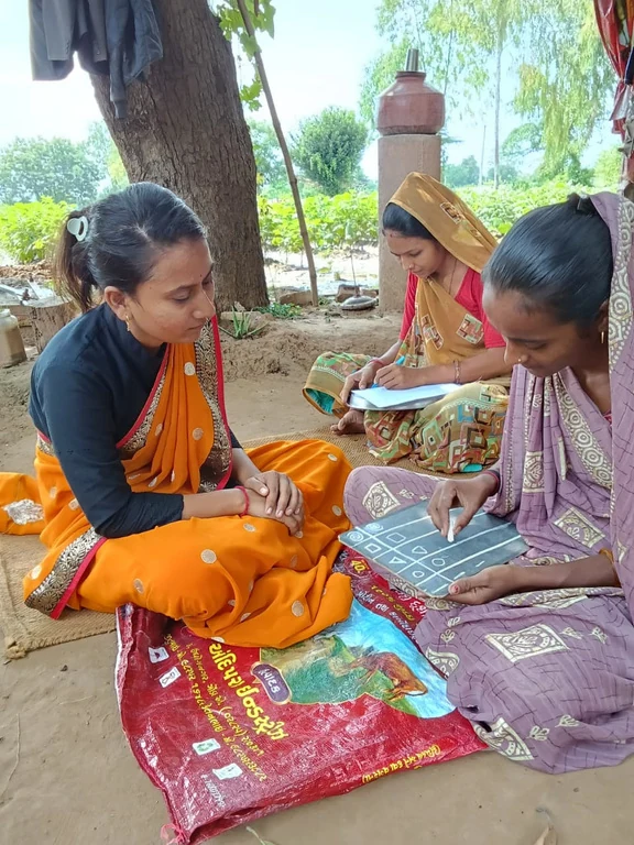 An educator supporting a woman as she practises writing on a slate during a literacy activity
